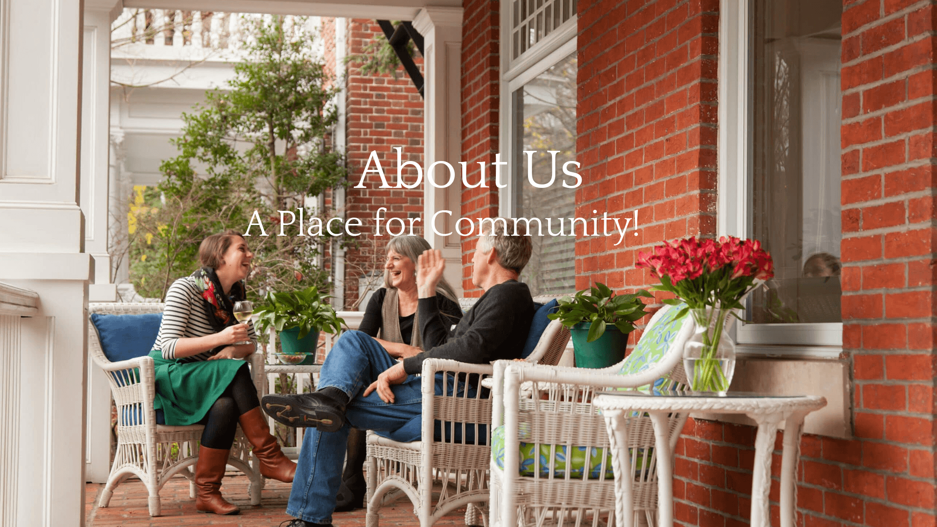 Three people enjoying conversation on a porch surrounded by plants and flowers.