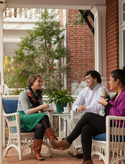 Three friends enjoy tea and laughter on a cozy porch.