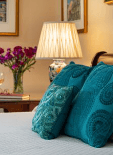 A cozy bedroom setting with decorative teal pillows, a lamp, and a vase of flowers.