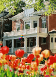 A brick house with a white porch is surrounded by colorful tulips and balloons.