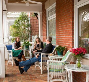 Three friends enjoying coffee on the front porch of the brick sided inn.